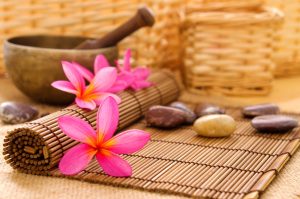 Health spa setting, low light with ambient. Frangipani, hot and cold stone on bamboo mat.